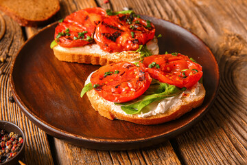 Plate of sandwiches with tasty grilled tomatoes and arugula on wooden background