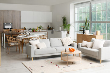 Interior of light open space kitchen with cozy grey sofas and oranges on wooden coffee table