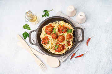Frying pan of boiled pasta with tomato sauce and meat balls on white table
