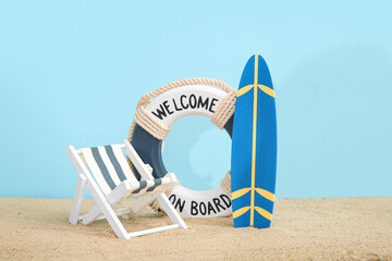 Creative composition with miniature surfboard, deckchair and life buoy on sand against blue...