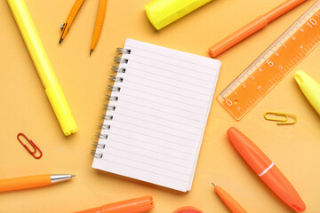 Notebook with different school stationery on orange background