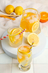 Glasses and jug of infused water with lemon on white tile background