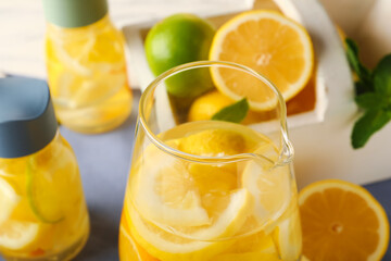 Jug of infused water with citrus fruits on table, closeup