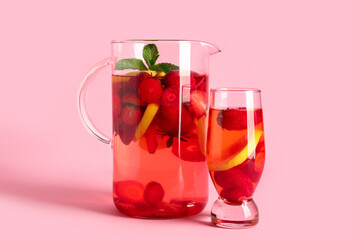 Glass and jug of infused water with strawberry on pink background
