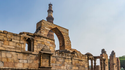 Ruins of the ancient temple complex Qutub Minar.  Dilapidated walls, arches, columns. The world's tallest brick minaret against the blue sky. Delhi. India. 