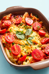 Baking dish of pasta with tomato sauce and cheese on blue background