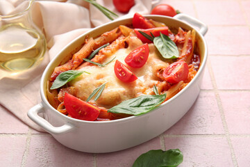 Baking dish of pasta with tomato sauce and cheese on pink tile background