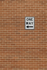 One Way road sign featuring text and bold black arrow icon fastened to a brick wall. The...