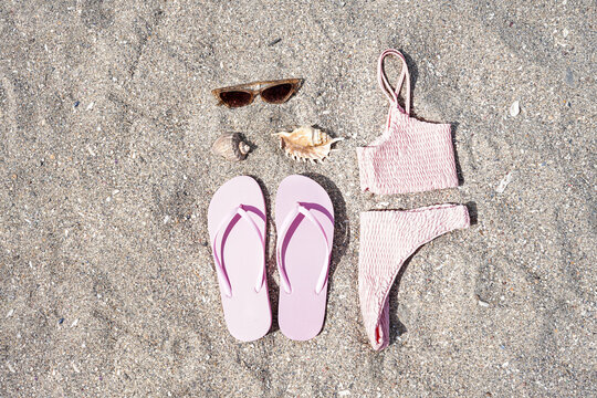 Pink flip-flops with swimsuit, sunglasses and shells on sand beach background