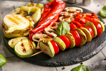 Board with tasty grilled vegetables on grey tile background