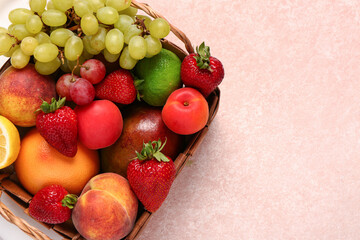 Wicker basket with different fresh fruits on pink background