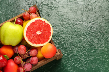 Wooden box with different fresh fruits on green table