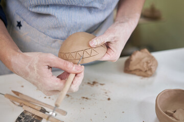 woman creates pattern on a clay pot by hands in artistic studio