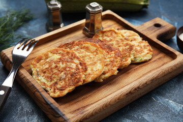 Wooden board of tasty zucchini fritters on blue background