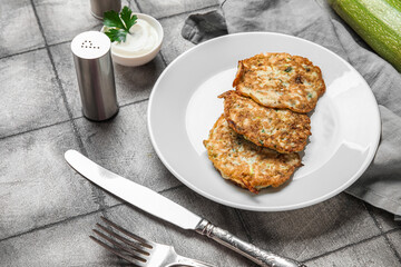 Plate of tasty zucchini fritters with sour cream on grey tile background