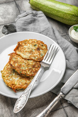 Plate of tasty zucchini fritters on grey tile background