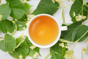 Cup of linden tea and leaves on white background