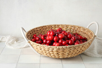 Wicker basket with sweet cherries on white tile table