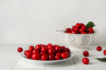 Plate and colander with sweet cherries on white tile table