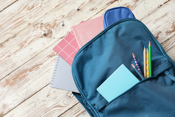 Naklejka premium Blue school backpack with notebooks and pencils on wooden background