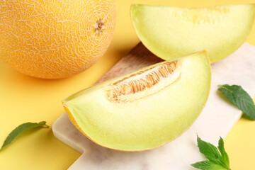 Board with pieces of sweet melon and mint on yellow background