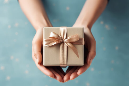 woman's hands hold brown present wrapping gift box with bright gold ribbon and bow