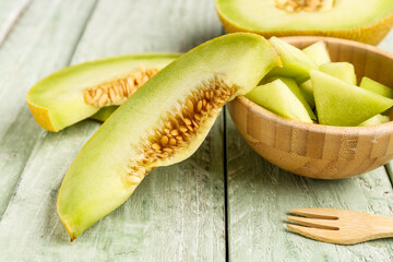 Bowl with pieces of sweet melon on green wooden background