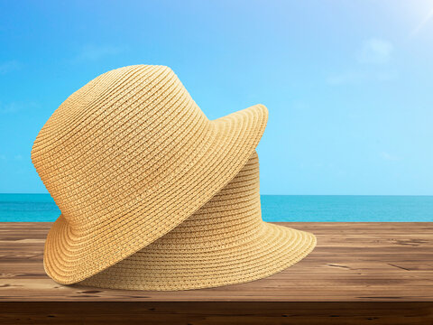 Two vintage straw hats lie on wooden table with sky and sea background.