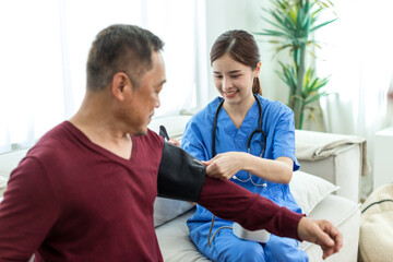 Fototapeta premium Caregiver nurse measuring blood pressure by using digital sphygmomanometer Senior patient at home. Caregiver nurse using medical device to measure blood pressure Senior patient.