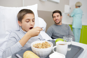 boy with breakfast in bed in hospital with his father