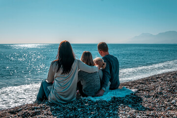 A family with children sits on the beach in winter and looks out to sea.