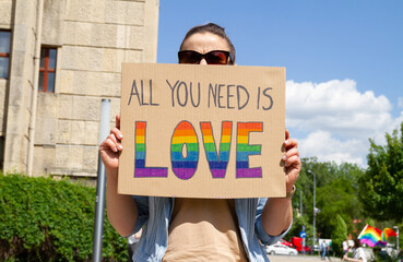 Girl holding placard sign All You Need Is Love with rainbow flag, during Pride parade. People at...