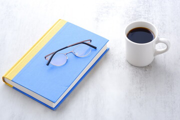 テーブルに置かれた一冊の本とメガネ、コーヒーのマグカップ