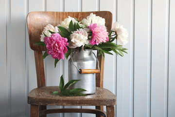 Still life with a bouquet of peonies in an aluminum can on a chair.