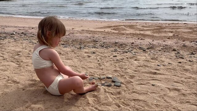 Little cute girl by the sea. Child playing in the sand on the beach