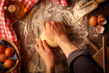 Baker knead pasta dough with hands on kitchen table background working with flour and eggs. Top...