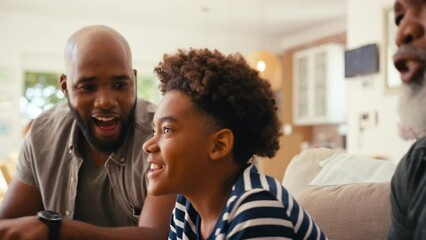 Close up of multi-generation male family sitting on sofa at home holding controllers playing video game together - shot in slow motion