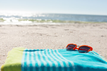 Red sunglasses on green and blue striped towel on sunny sand beach by the sea, copy space