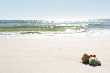 Fototapeta na wymiar Red sunglasses, sunhat and rolled beach towel on sunny sand beach by the sea, copy space