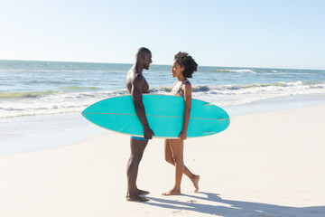 Obraz premium Happy african american couple holding surfboard smiling at each other standing on sunny beach