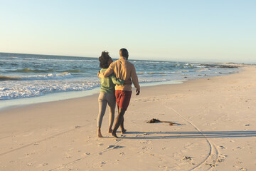 Happy african american couple embracing and walking on sunny beach by the sea