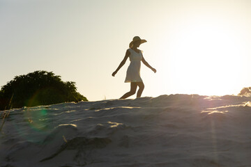 Happy african american woman in sunhat and beach dress dancing on beach at sunset, copy space
