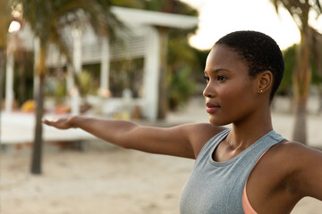 Focussed african american woman practicing yoga standing with arms outstretched on beach at sundown