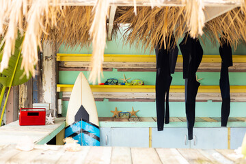 Counter of sunny surf hire shop on beach with radio, surfboard and hanging wetsuits