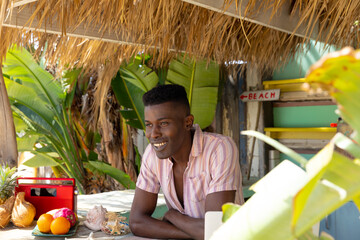 Portrait of happy african american man leaning on counter of surf hire beach shack