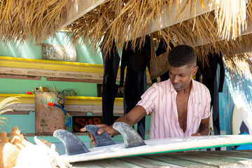 Focussed african american man preparing surfboard behind counter of surf hire beach shack