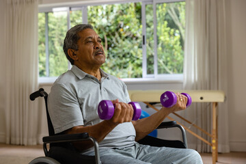 Determined senior biracial male patient in wheelchair using dumbbells - Powered by Adobe