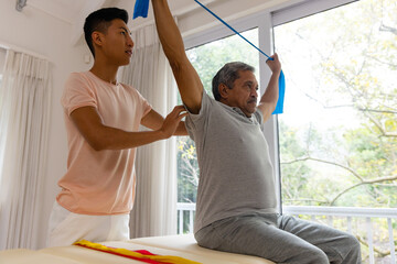 Fototapeta premium Diverse male physiotherapist advising and senior male patient using exercise band