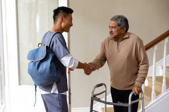 Diverse male doctor and senior male patient with crutches shaking hands at home