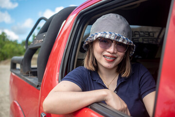 A young intrepid and adventurous woman in the open rear seat of a red pickup truck. An expedition...